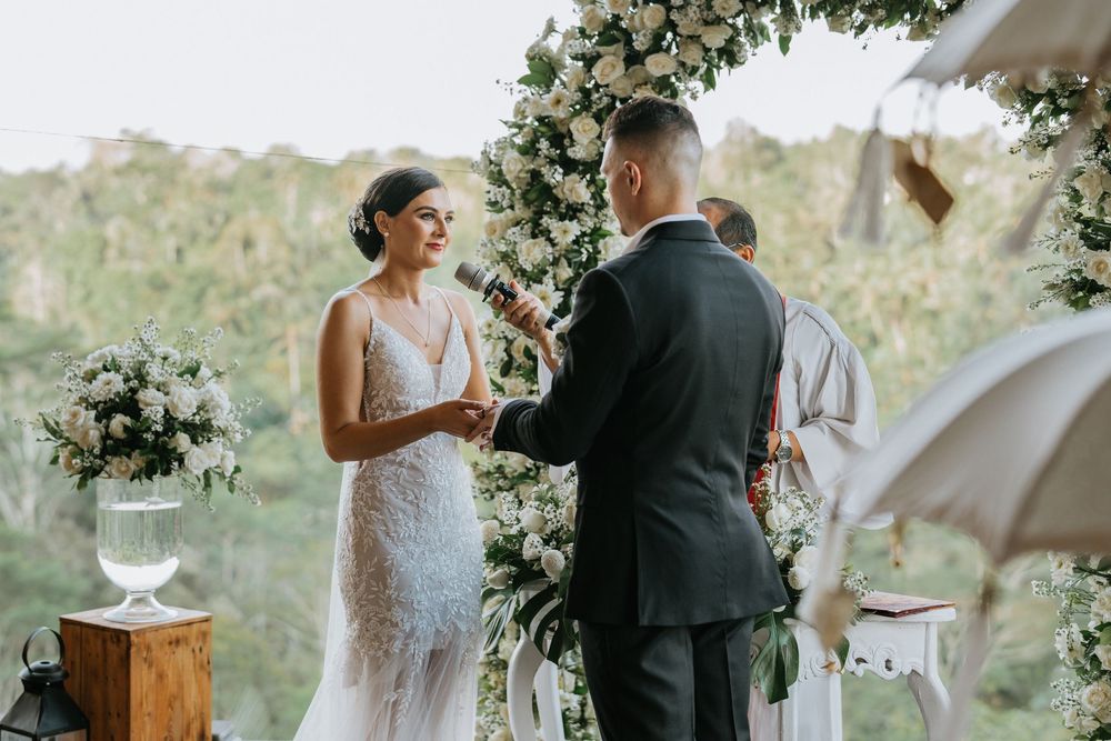 Wedding ceremony under a floral arch with white drapery outdoors.