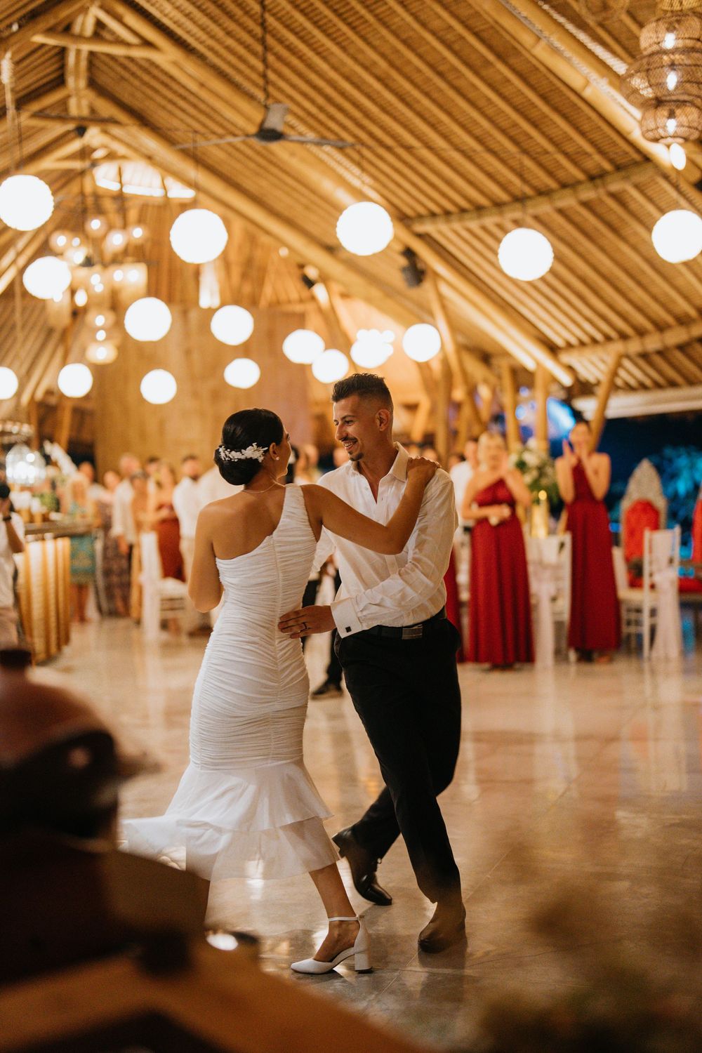Couple dances in rustic venue decorated with hanging lights.