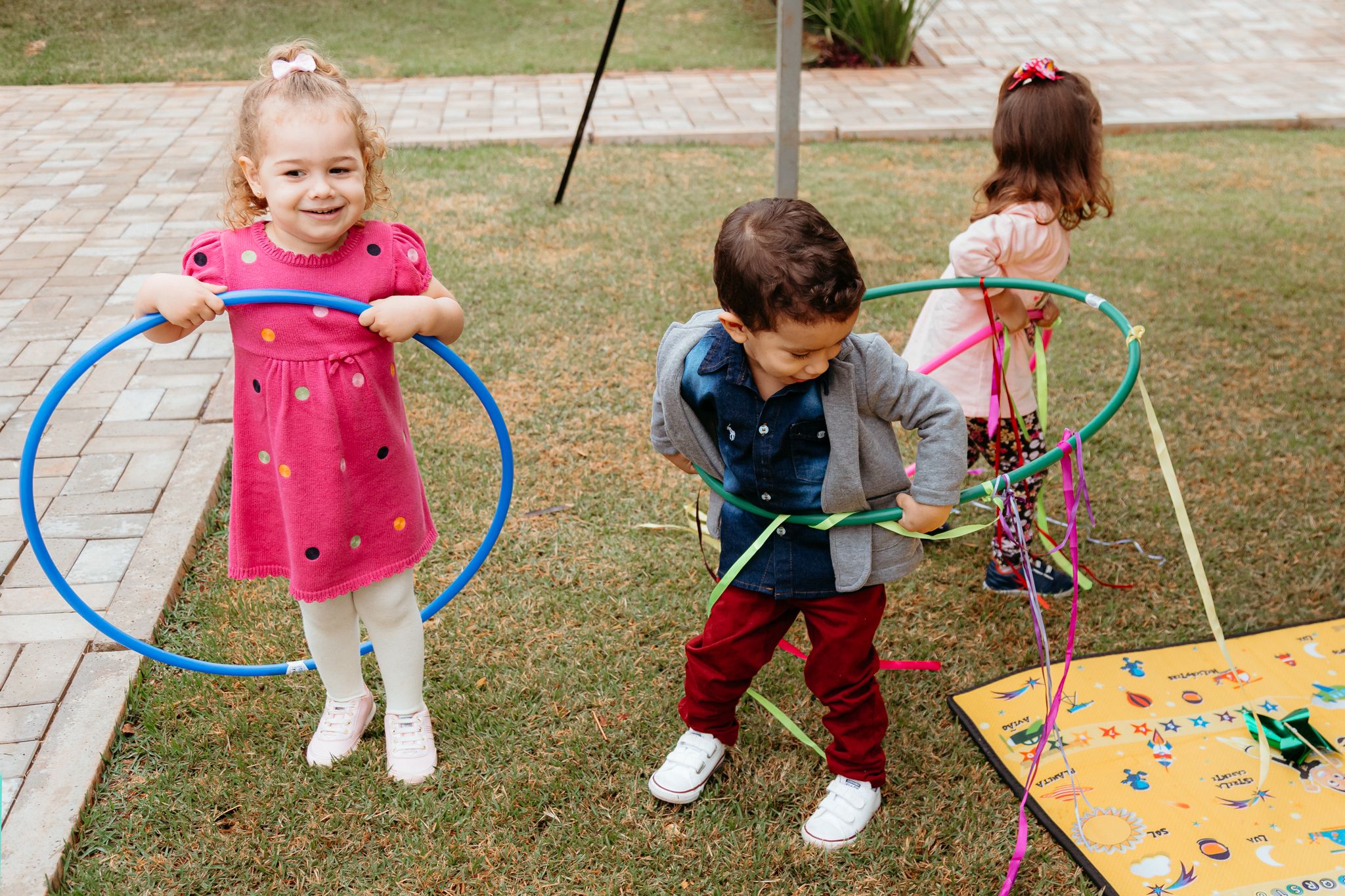 Young children play outdoors with colorful hula hoops and physical activity equipment on a sunny day.