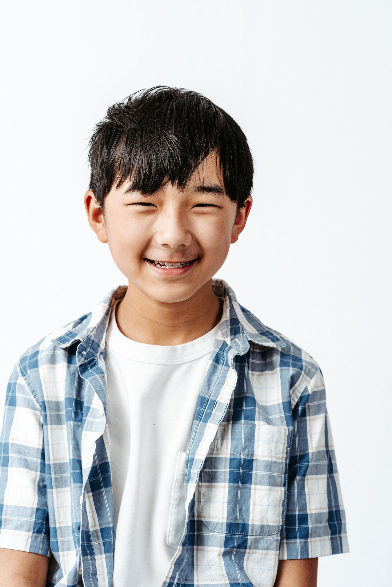 Smiling child wearing blue and white plaid shirt and white t-shirt shown in three similar poses against white background.