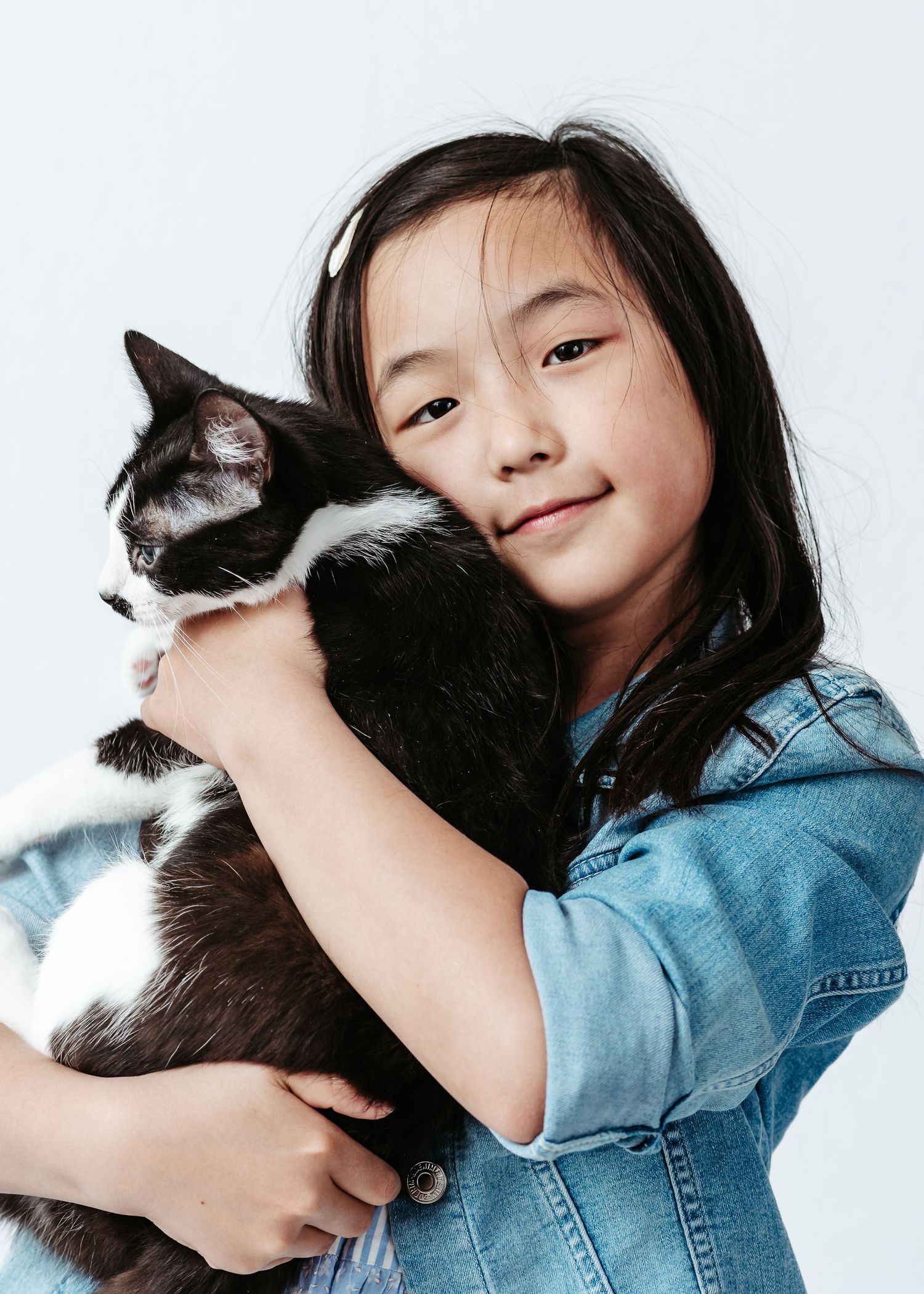 Young child in denim holding and cuddling with black and white cat shown in sequence of poses against white background.
