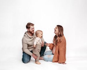Parents and baby playing together on white background in matching brown and beige outfits.