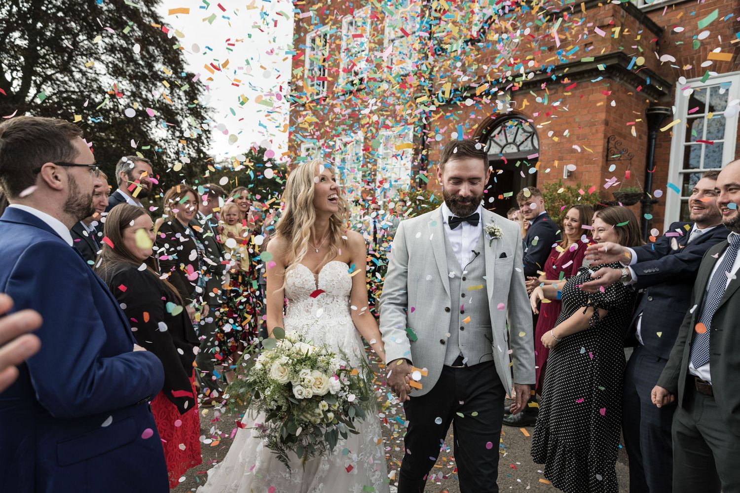 Wedding guests throwing confetti on the steps of Kelham House as the bride and groom smile