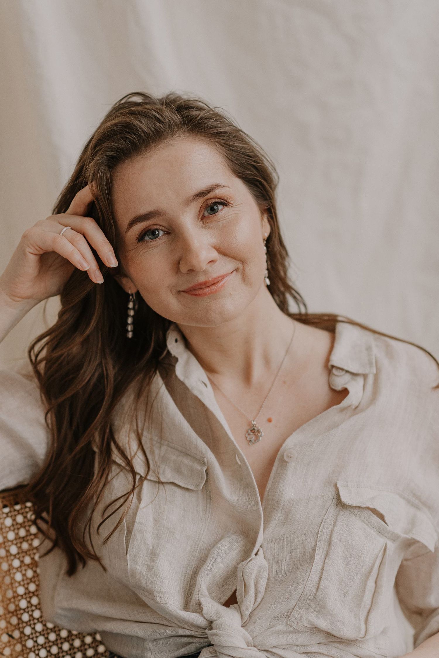 Soft portrait in beige linen shirt with delicate jewelry details.