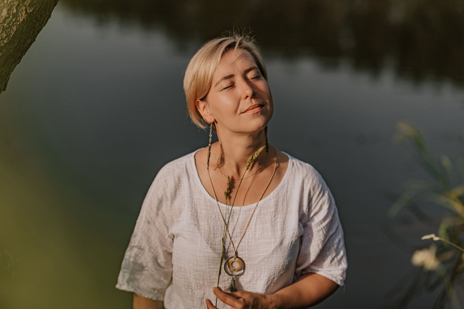 A figure relaxes thoughtfully on a blanket in a sunlit meadow surrounded by trees.