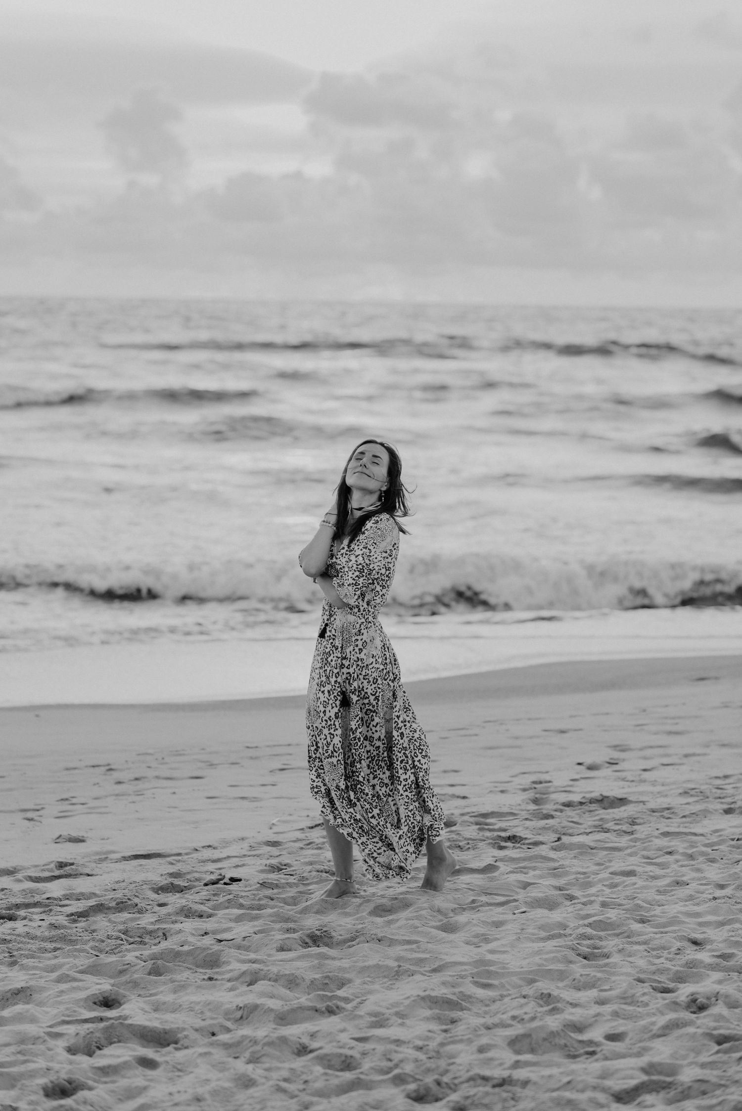 Black and white photo of someone dancing joyfully on a beach with waves in the background.