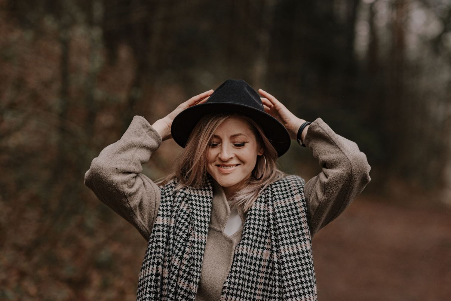A vintage-inspired autumn scene with someone adjusting their hat among fall foliage.