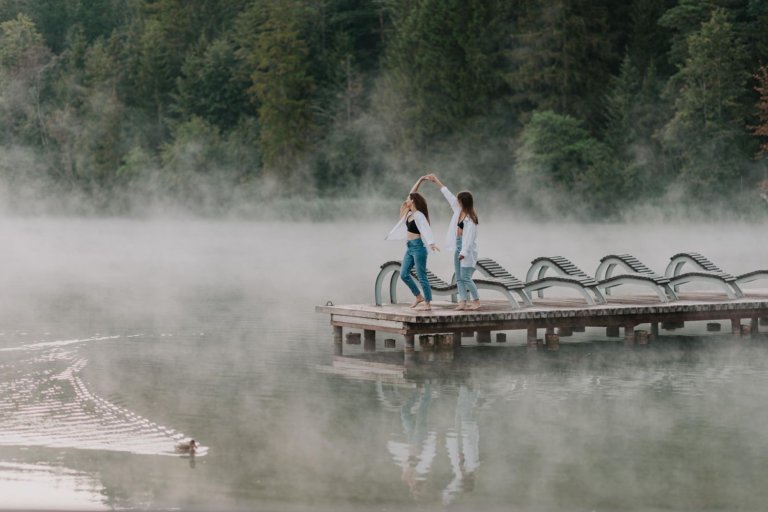 Friends pose playfully on a misty lake dock with mountain forest backdrop.