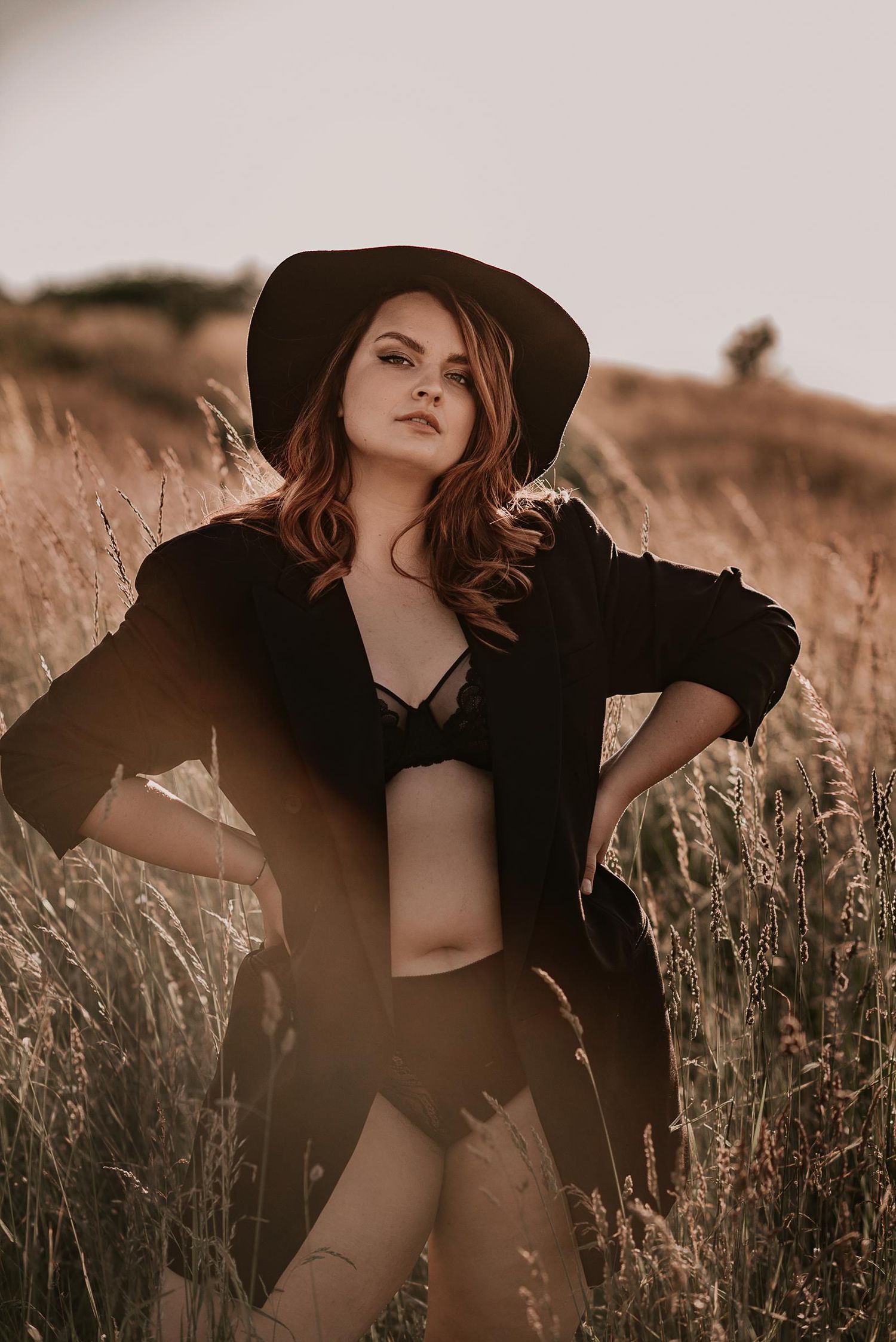 Dramatic sunset portrait in golden wheat field with black hat and flowing fabric.