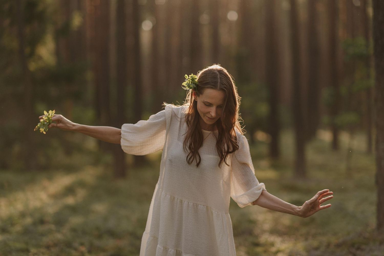 Ethereal scene of someone in a flowing white dress dancing in a pine forest.