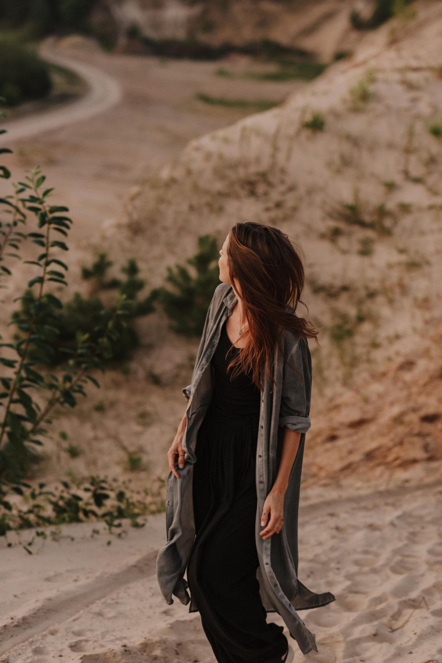 Figure in black clothing moves expressively against a sandy landscape at sunset.