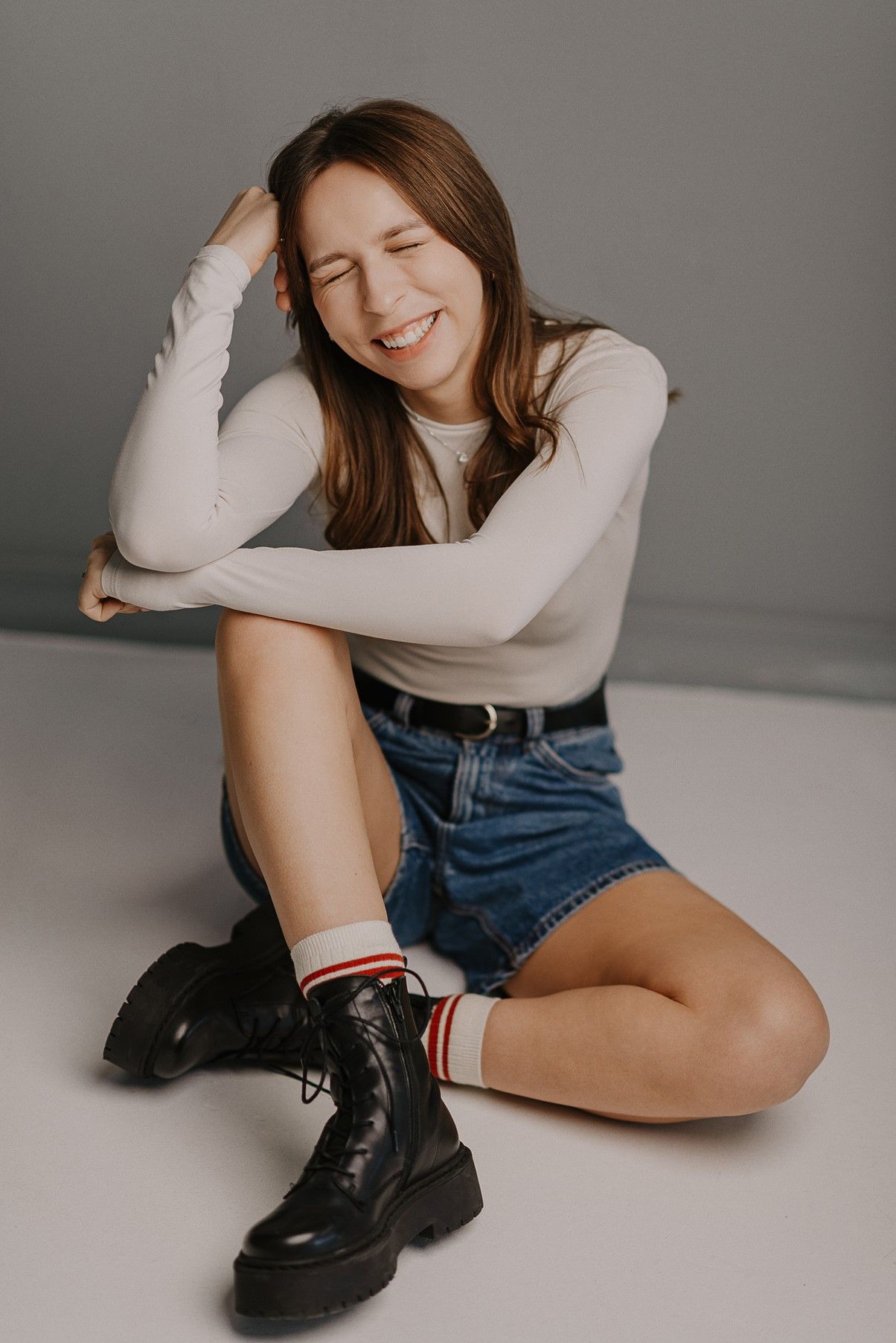 Casual style portrait with white top, denim shorts and black combat boots on a grey background.