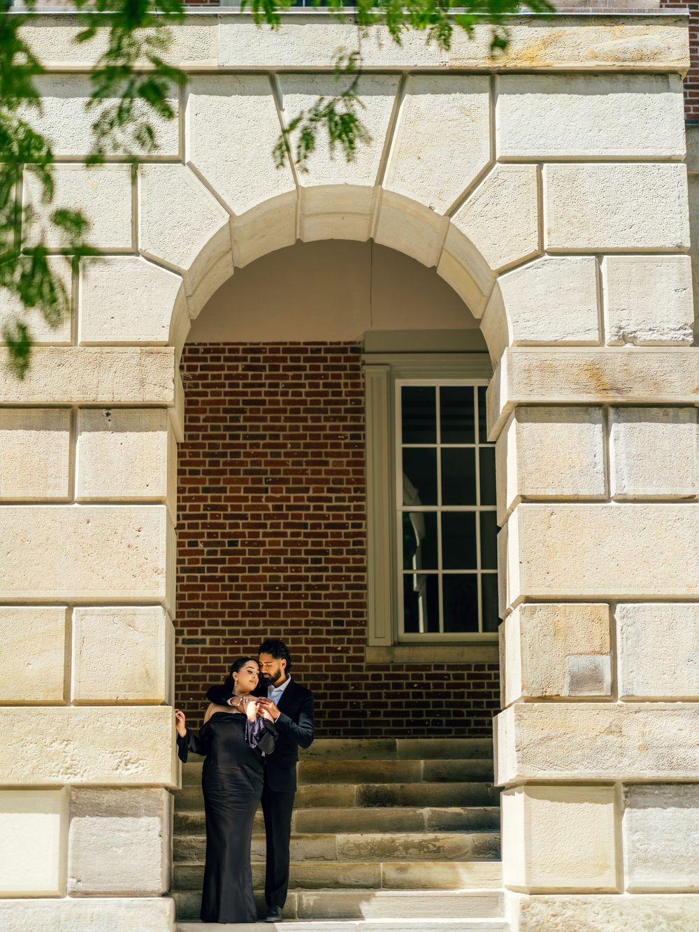 A romantic couple shares an intimate moment in an arched stone doorway of a historic building.