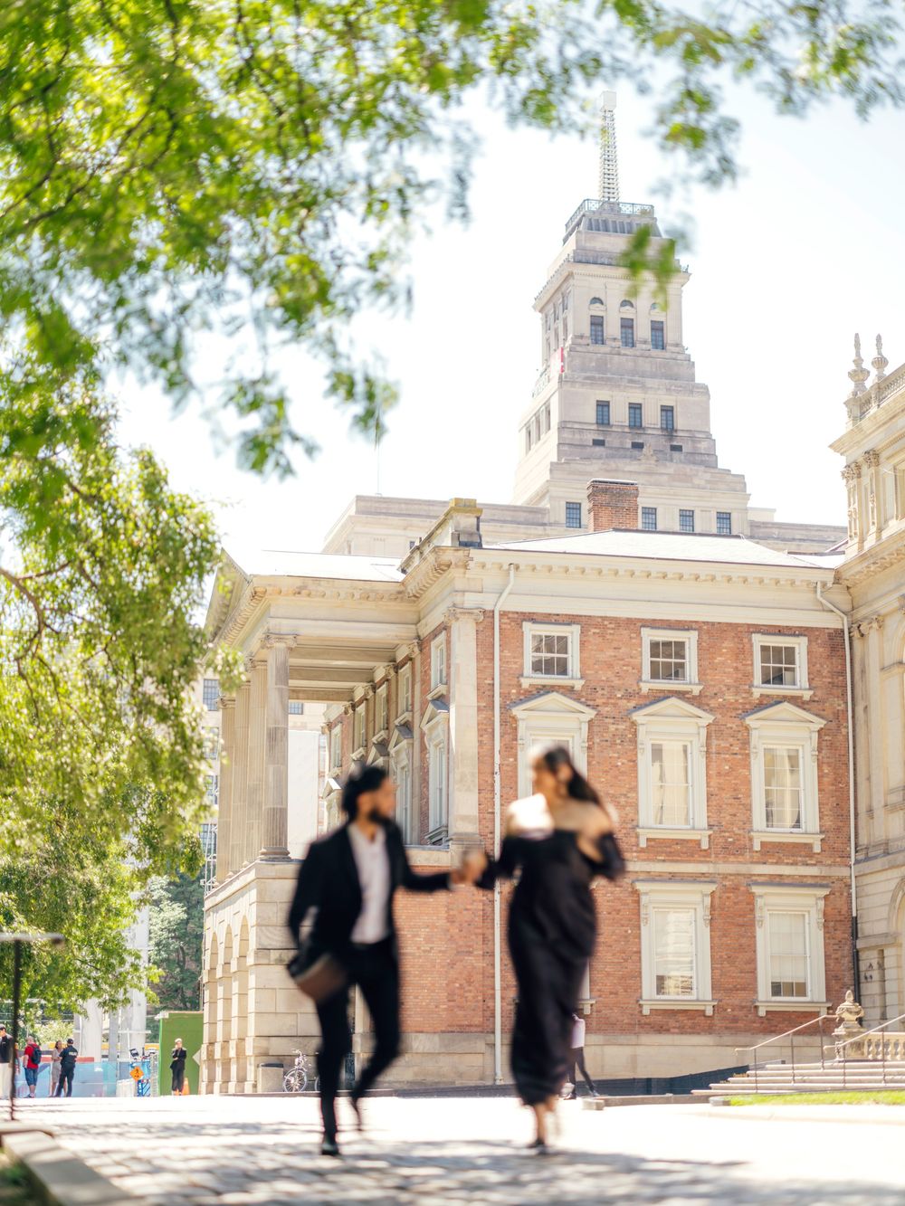 Silhouettes of dancing figures against the backdrop of a historic brick building with classical architecture.