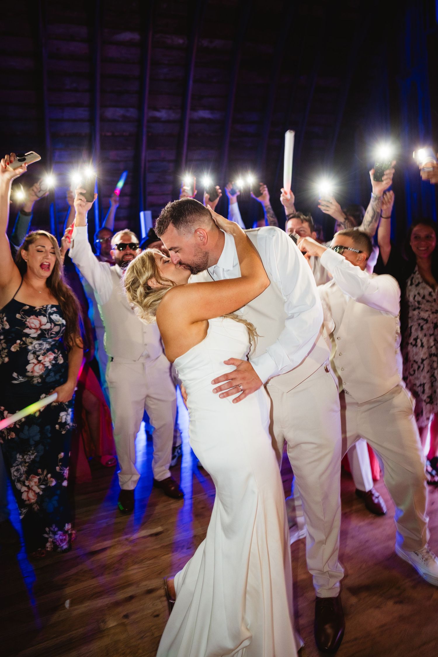 Wedding party dances enthusiastically together on the reception dance floor with colorful lighting and festive atmosphere.