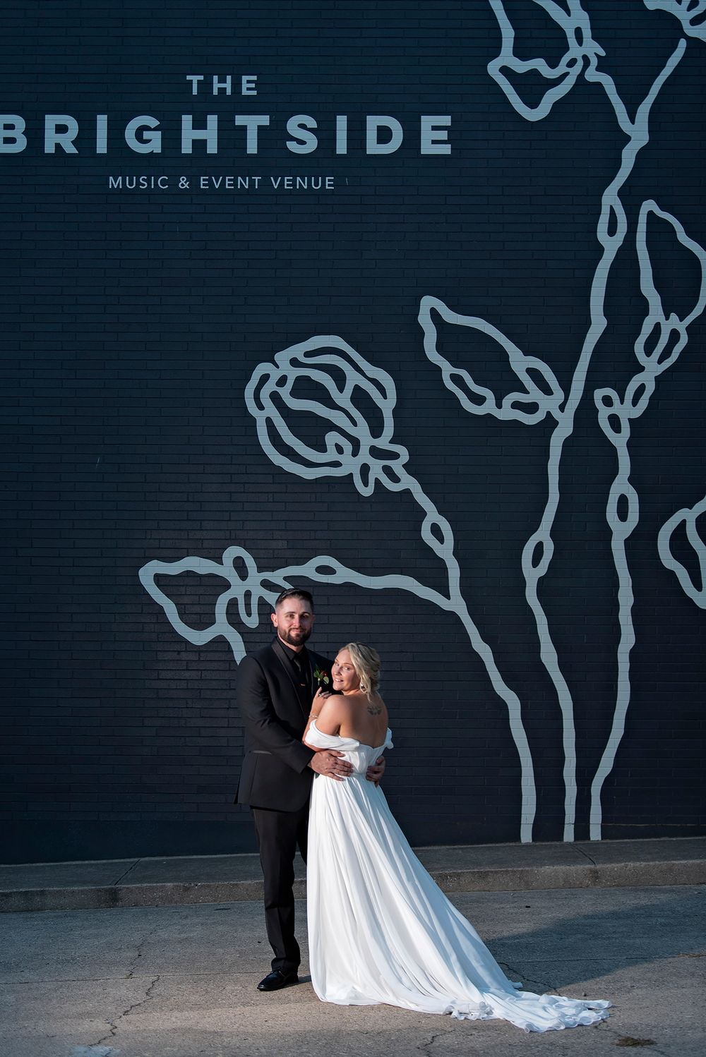Wedding couple poses against dark wall with artistic tree designs at The Brightside venue.