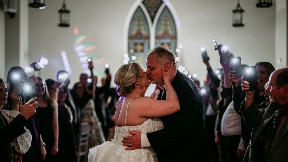 A panoramic view of a wedding celebration with dancing silhouettes against a candlelit reception venue backdrop.