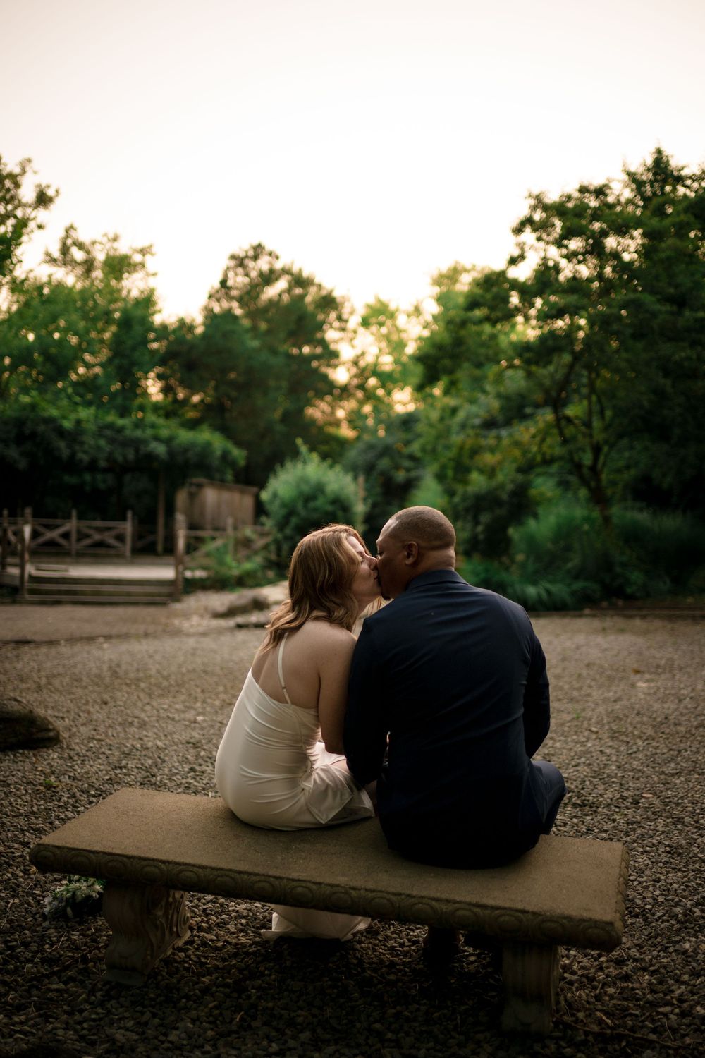 Couple sits intimately together on wooden bench at sunset in a peaceful outdoor park setting.
