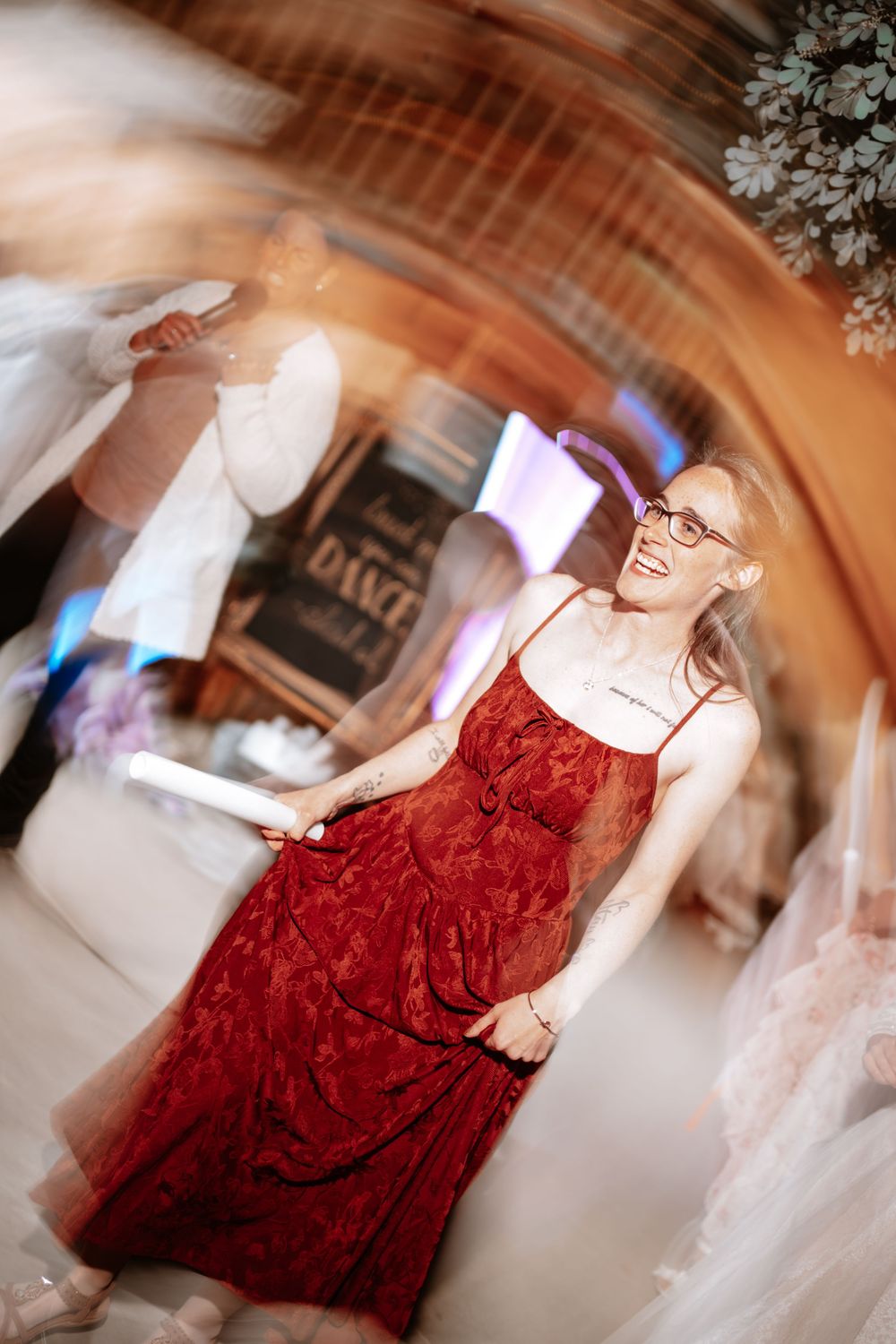 Woman in red lace dress smiling at a wedding reception dance floor with floral decor.