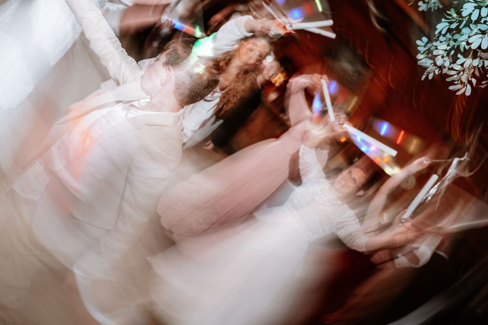 Blurred motion photo of bride dancing joyfully at wedding reception with colorful lights.