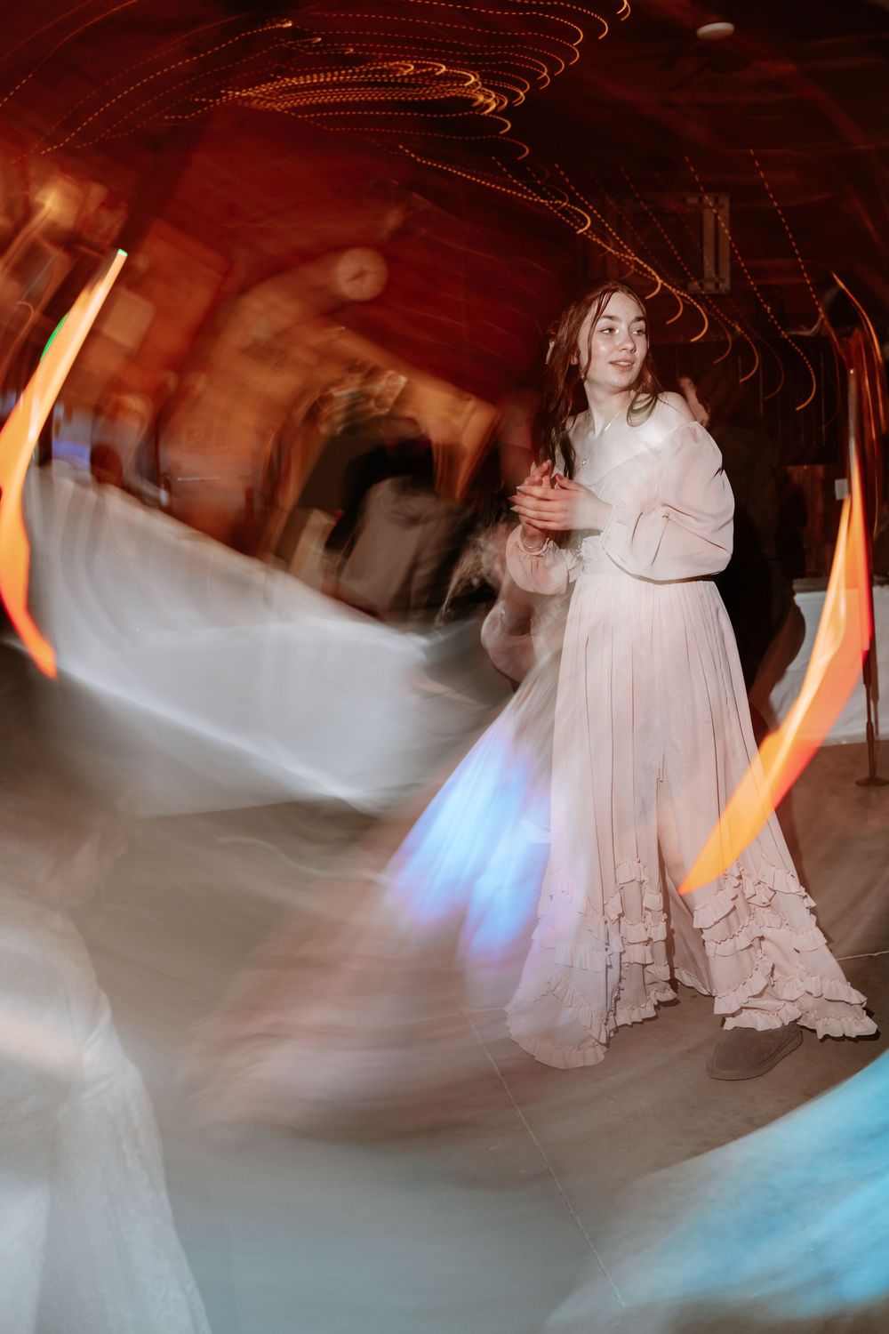 A bride in a white gown dances gracefully, captured with a long exposure effect showing swirling lights around her.