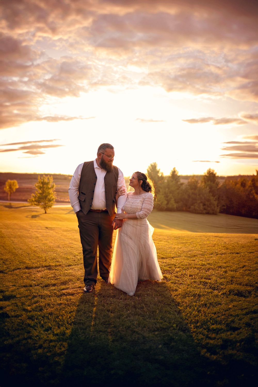 A bride and groom share a romantic moment at golden sunset on a lush green field during their outdoor wedding.