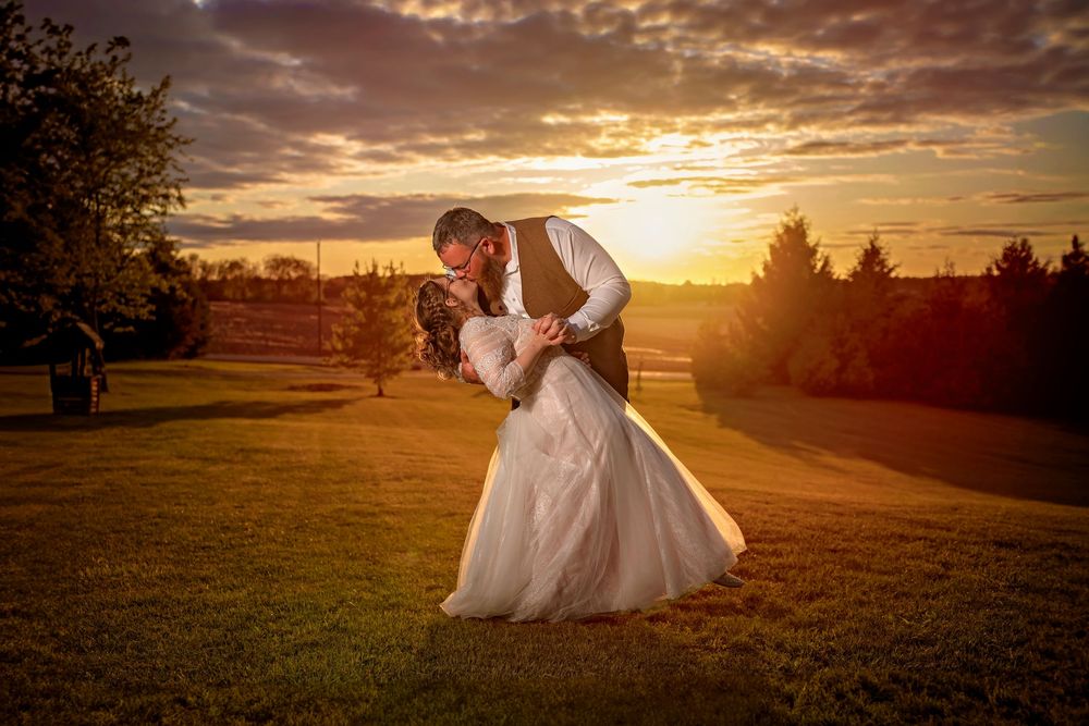 Bride and groom share a romantic dip kiss at sunset on a lush green lawn during their outdoor wedding.