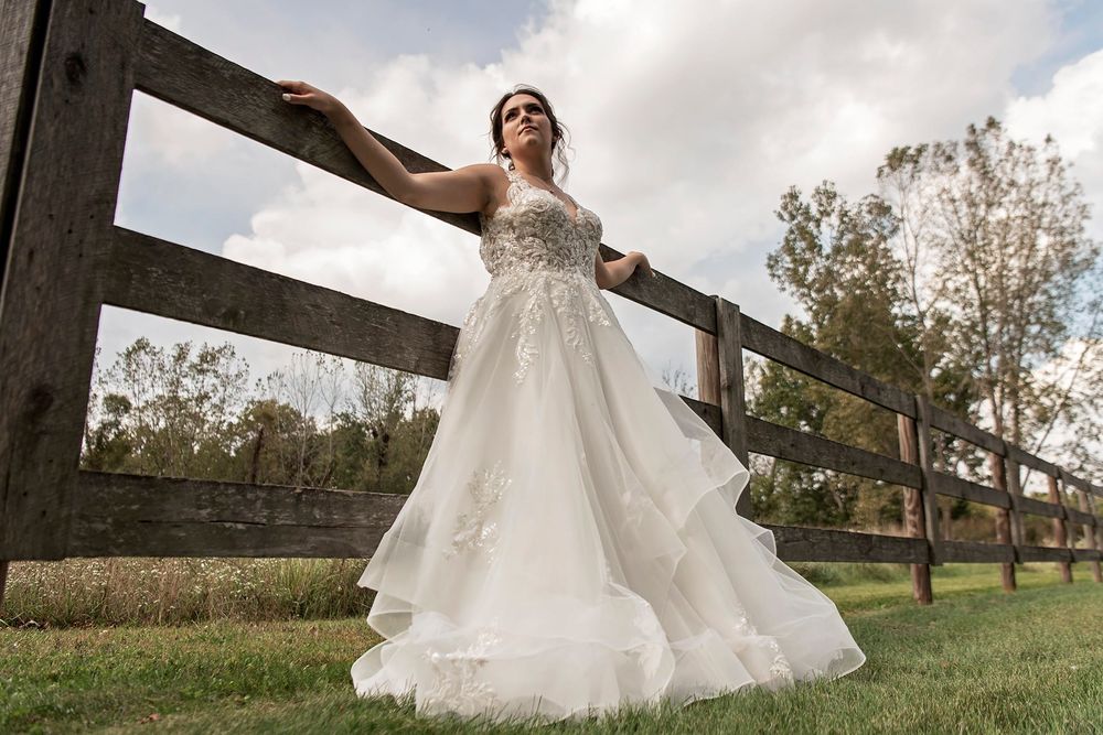 Bride in flowing white dress posing gracefully against rustic wooden beams outdoors.