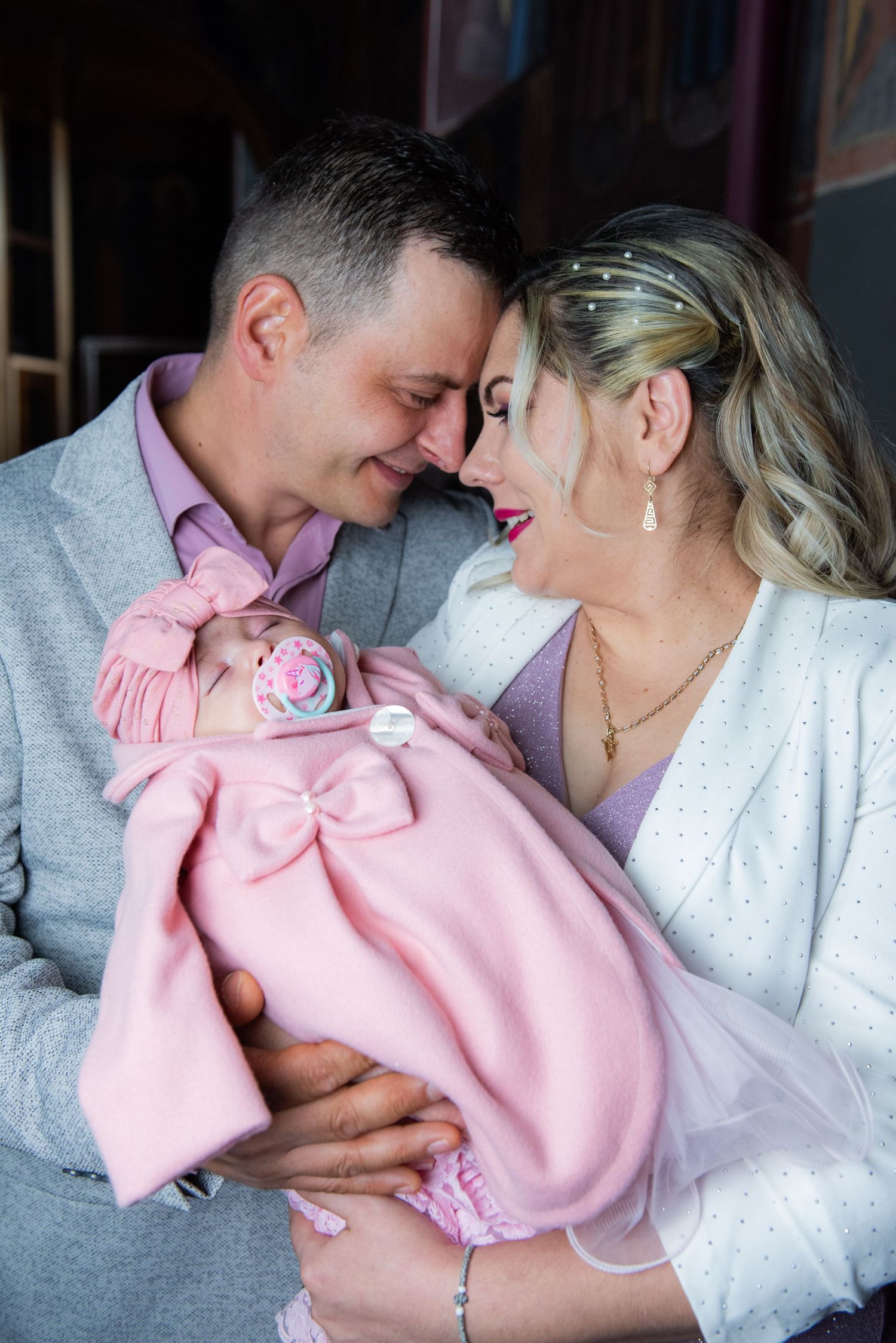 Couple in grey and white sharing intimate moments while holding baby in pink.