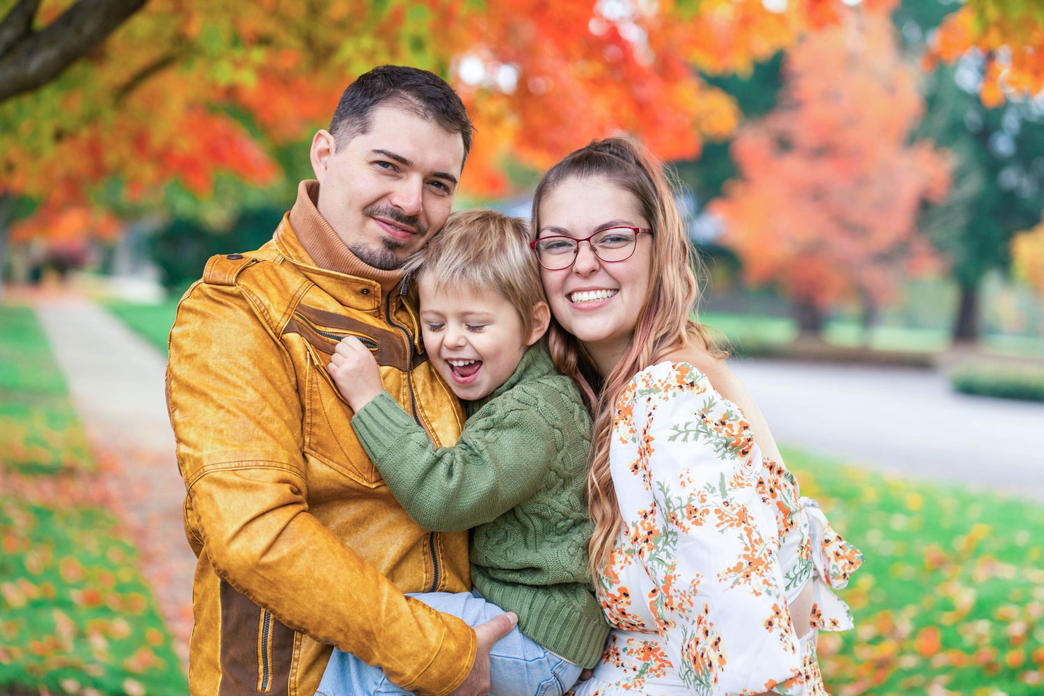 Fall family portrait with green and orange colors and the family of 3 hugging and laughing