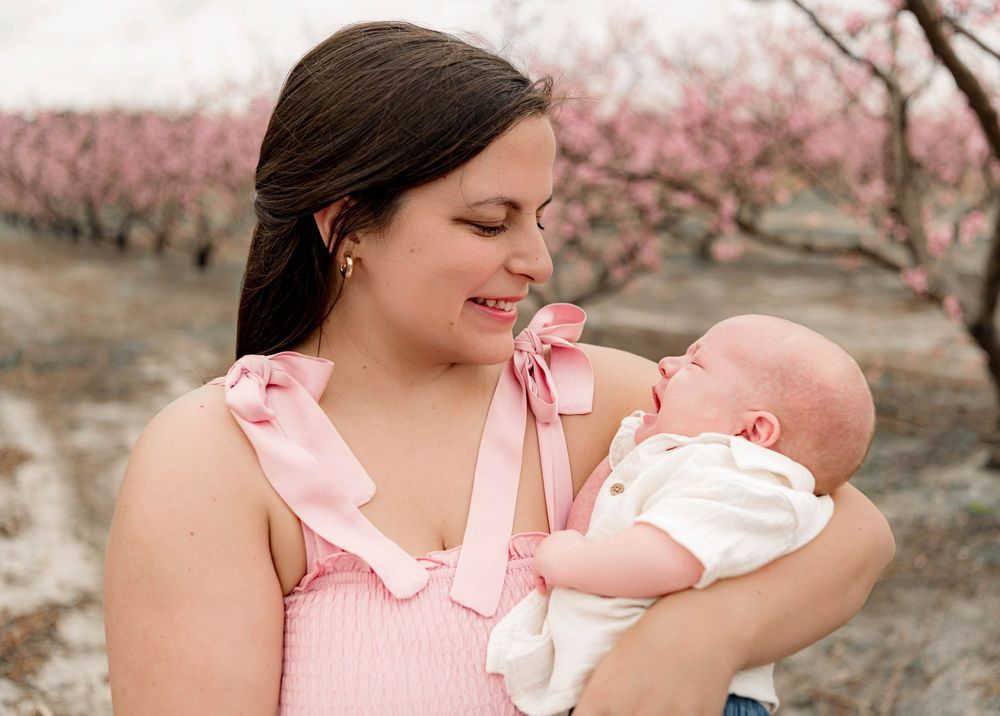 Mother and baby portraits in pink dress against blooming cherry blossom trees.