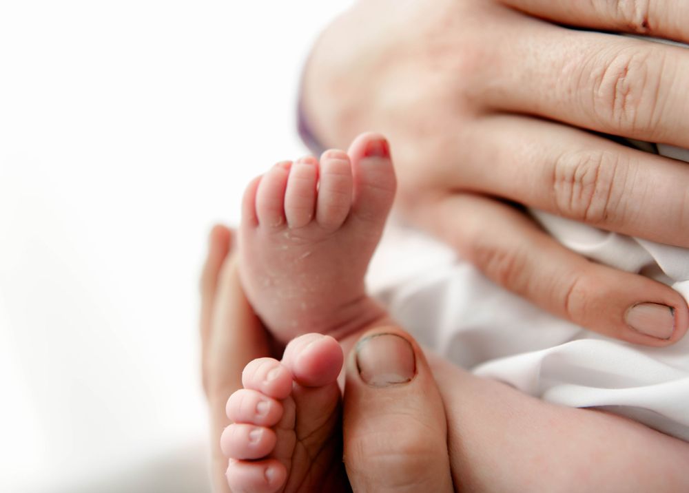 Close-up details of newborn baby's tiny feet and hands against white background.