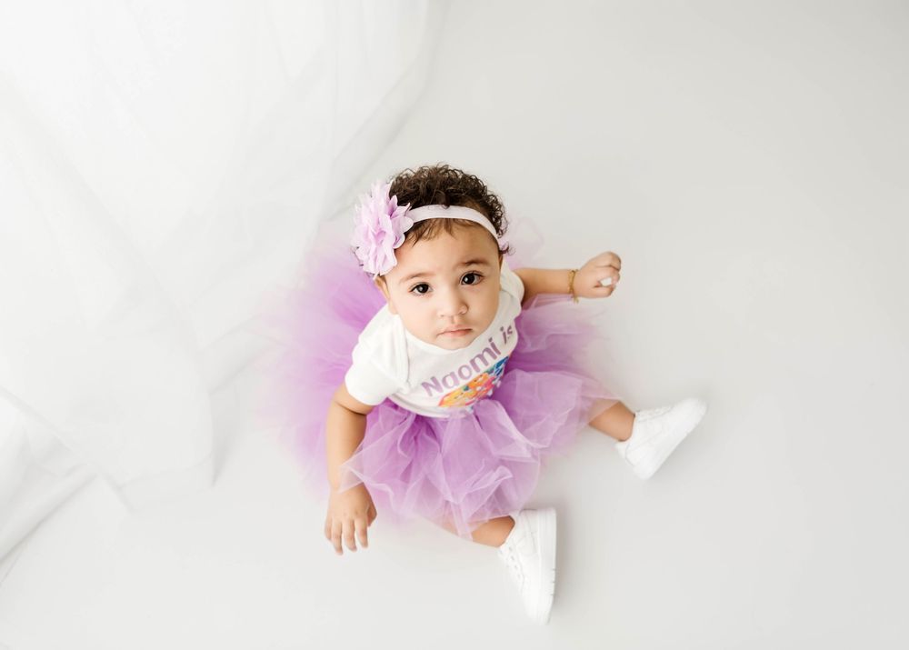 Baby in purple tutu crawling on white background.
