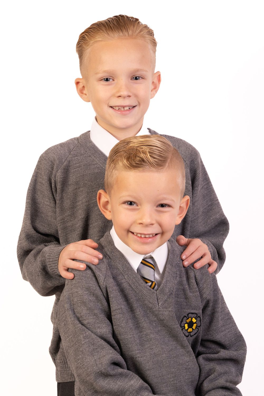 Two students in grey school uniforms pose together for playful studio portraits.