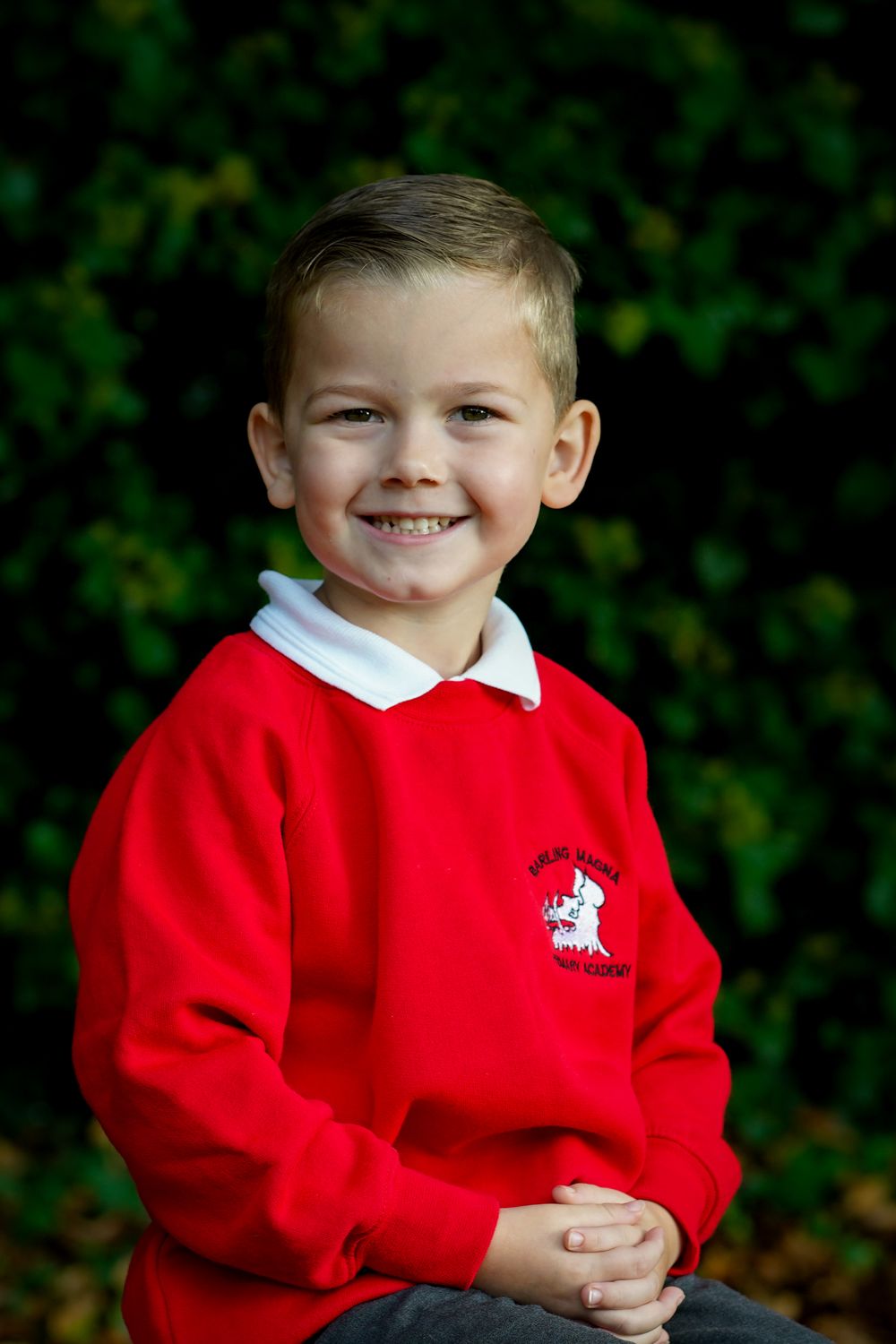 Child in bright red school jumper with white collar and school logo smiles at the camera.