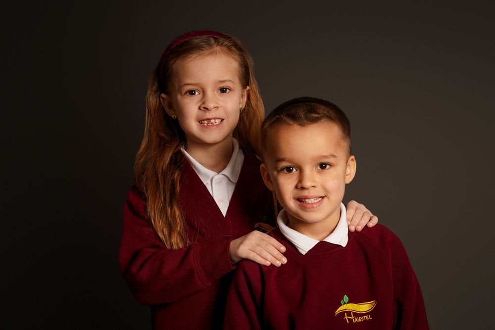 Students in burgundy uniforms pose together against a dark studio background.