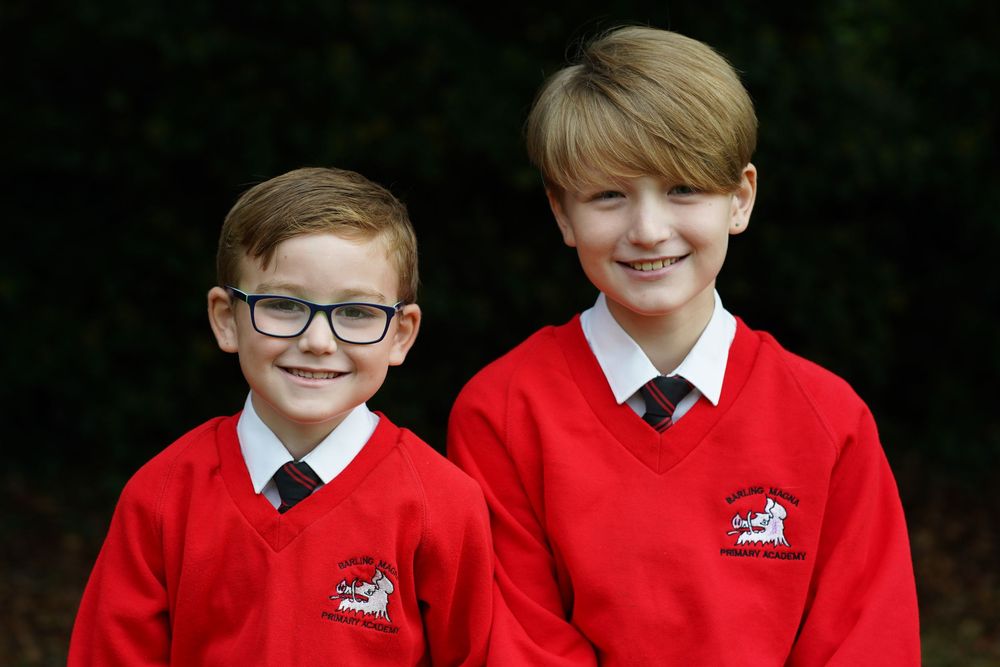 Students in red school sweaters with white collars pose against a natural outdoor setting.