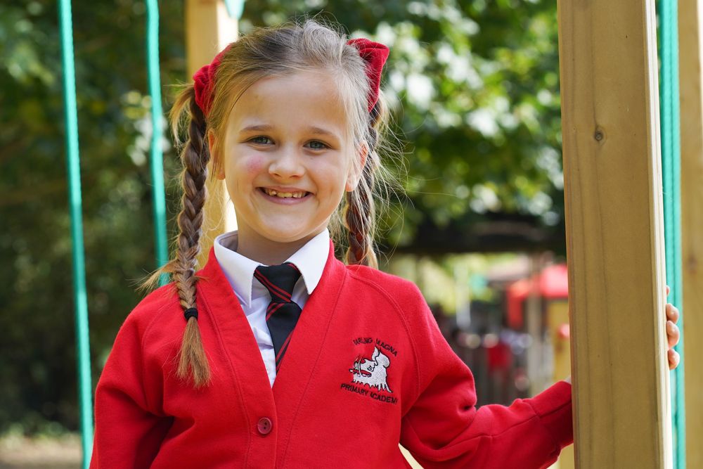 Students in red school uniforms stand near turquoise playground equipment outdoors.