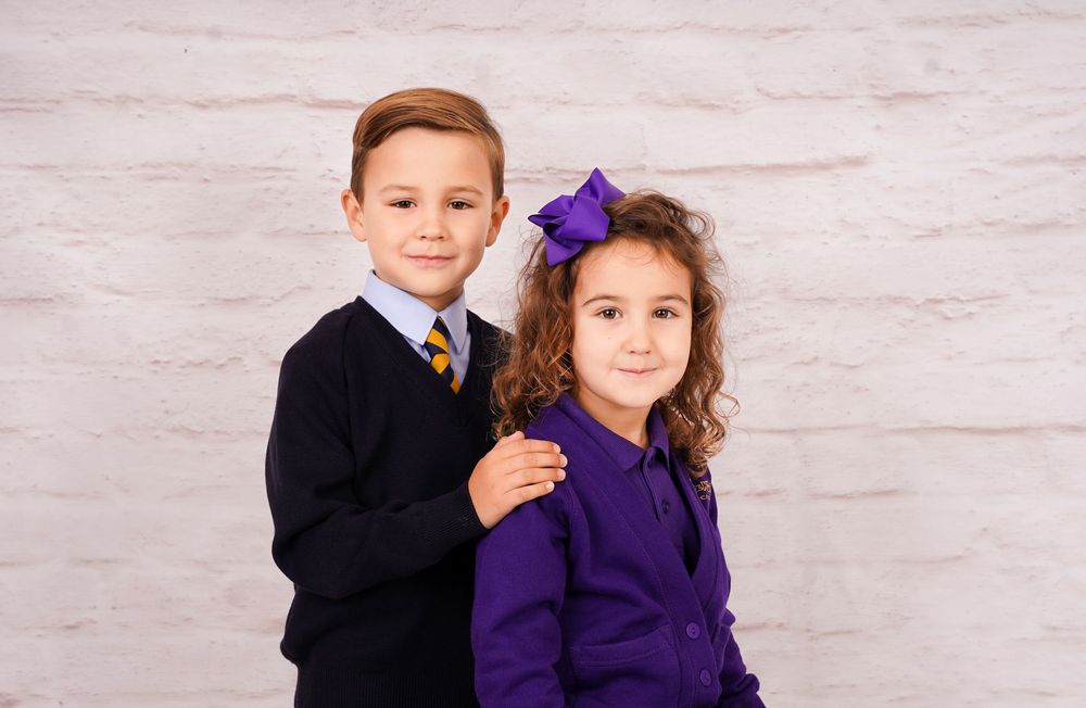 Students in formal school uniforms pose together against white studio background.
