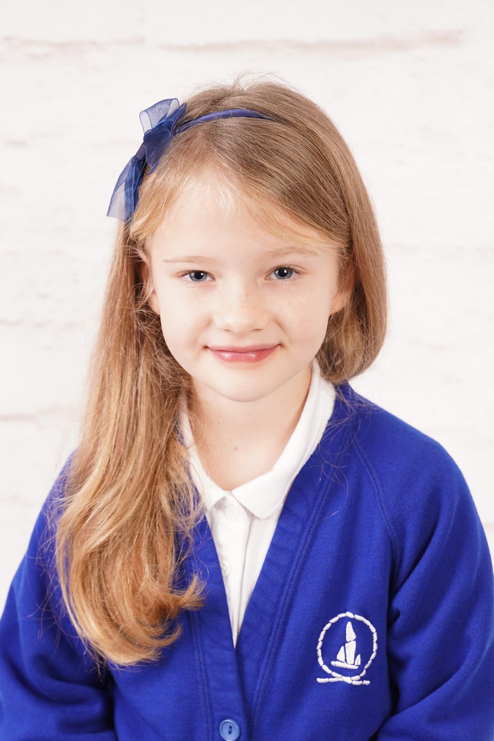 Student wearing royal blue school cardigan with school logo smiles in bright studio setting.