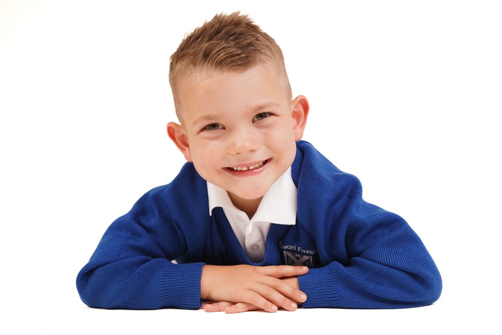 Student in navy blue school uniform lying down for casual portrait against white background.