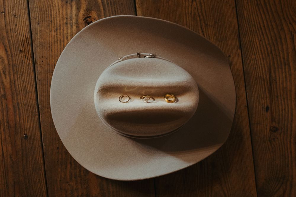 Gold wedding rings displayed on a tan cowboy hat resting on a rustic wooden surface.