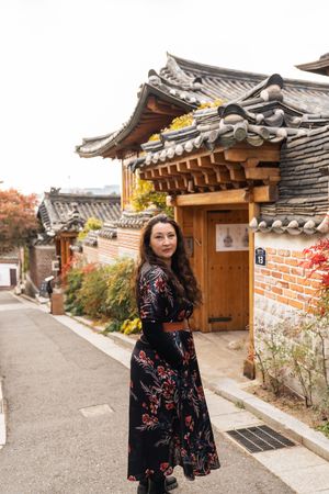 Woman in a black floral dress exploring traditional Korean hanok village streets in autumn.