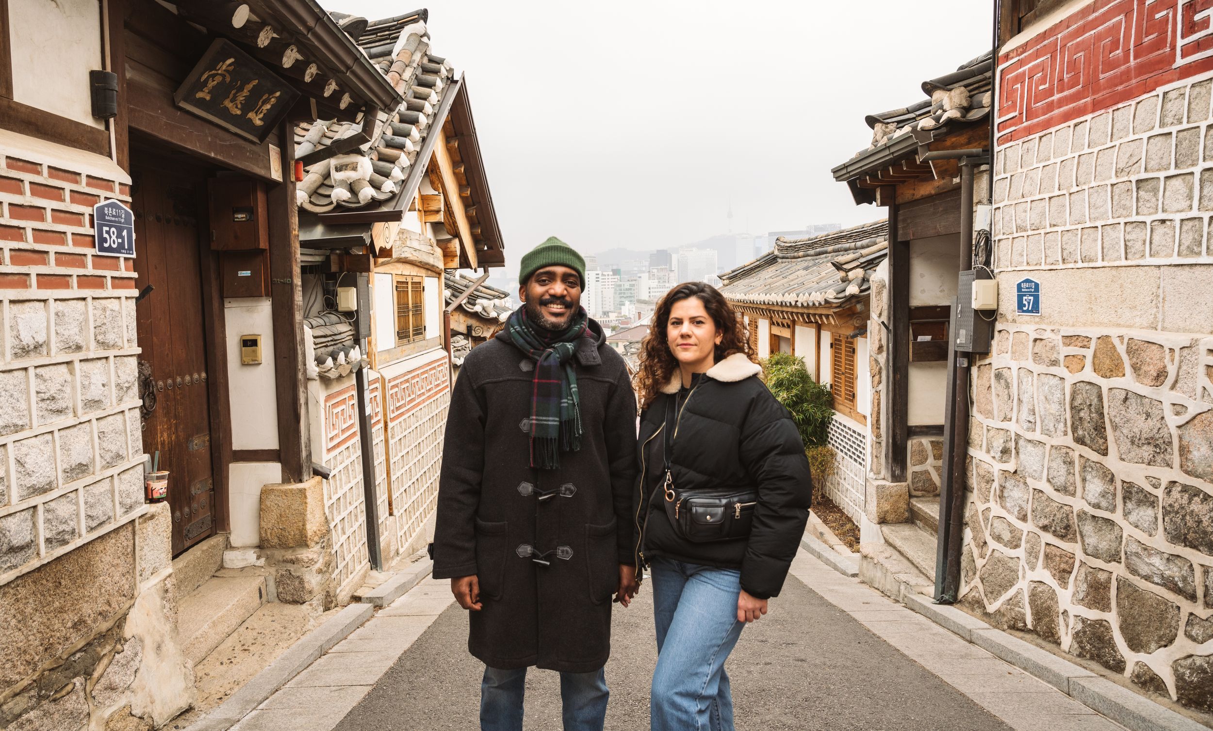 Tourists walk along narrow stone streets between traditional Korean houses in Bukchon Village.