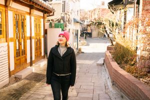 Person walking along peaceful traditional Korean hanok village street on a sunny day.