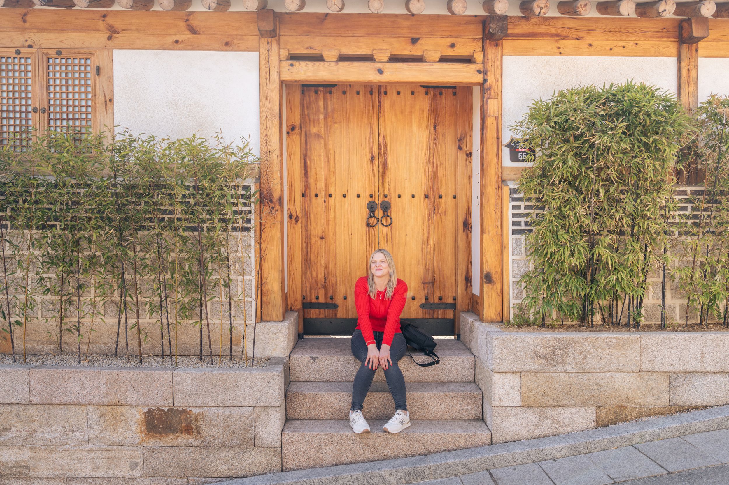 People resting on wooden benches against traditional Korean architecture and garden.