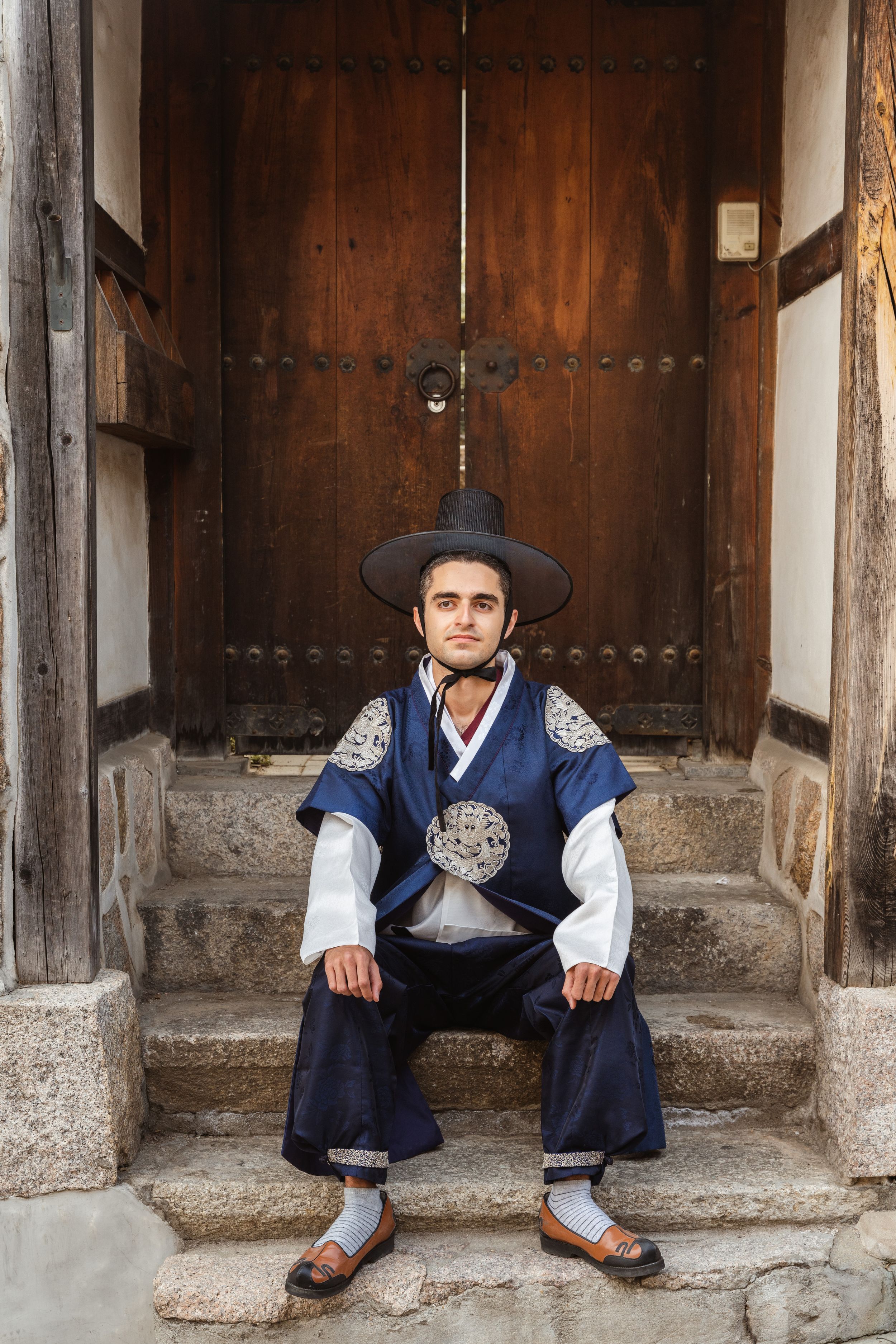 Traditional Korean hanbok-clad figure sits on wooden steps of historic building.