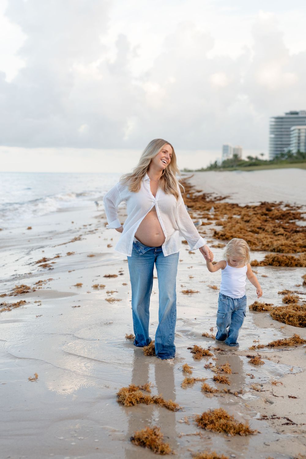 Parent and child playing together at the beach with seaweed and waves in the background.