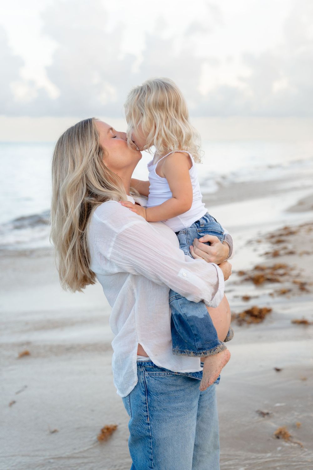 Two people share a tender moment on a serene beach during golden hour.