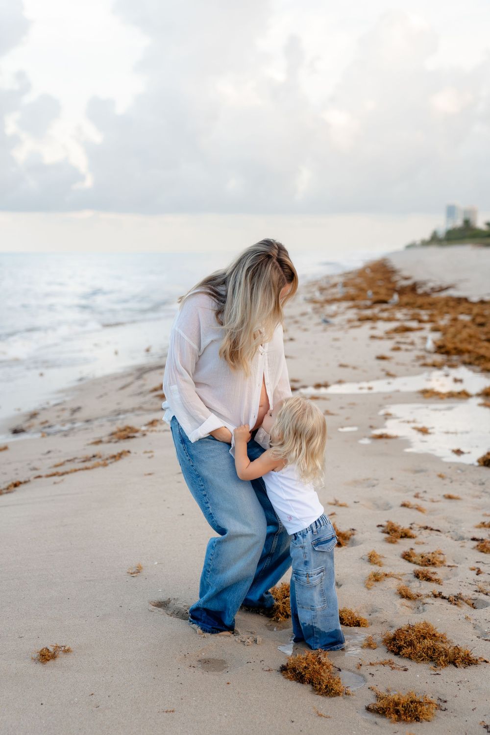 Two people share a tender moment while exploring seaweed washed up along a misty shoreline.